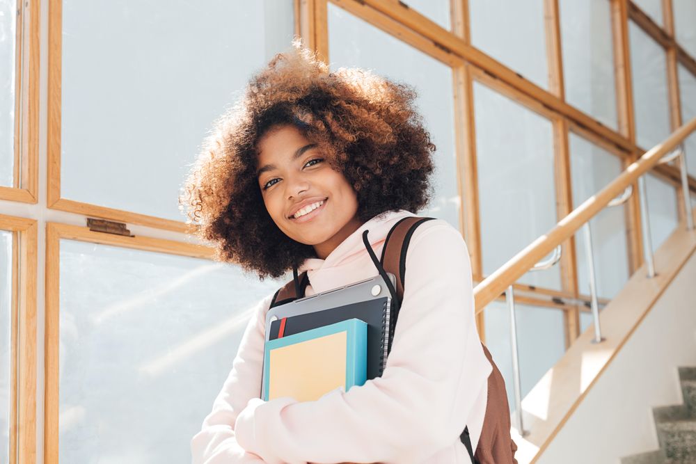 Teenage female student standing on stairs in school holding text books