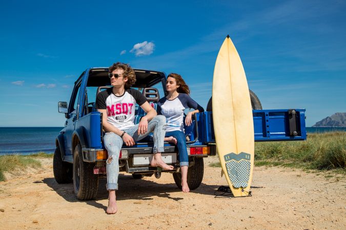 Couple with surfboard sitting on a car