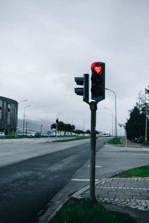 Red traffic light in heart shape against overcast sky, vertical