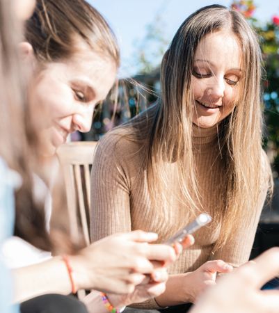 Young women taking a break from studying showing messages on phones while talking and laughing.