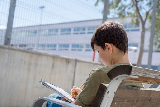 Back of teenager on bench outside drawing in notebook