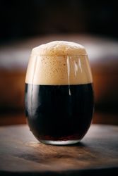Glass of fresh stout with froth on wooden table