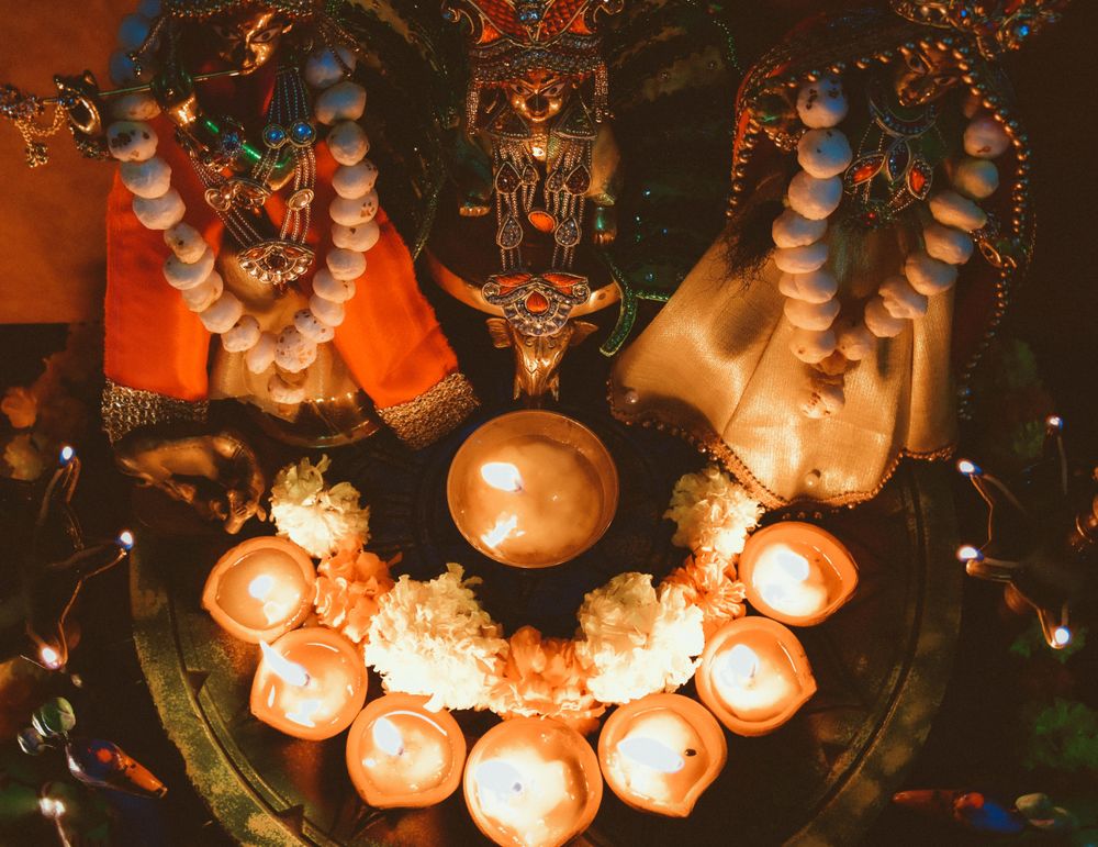 Lit diyas beside saffron flowers and Hindu deities on a table