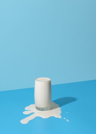 Overflowing glass of milk isolated on a blue background