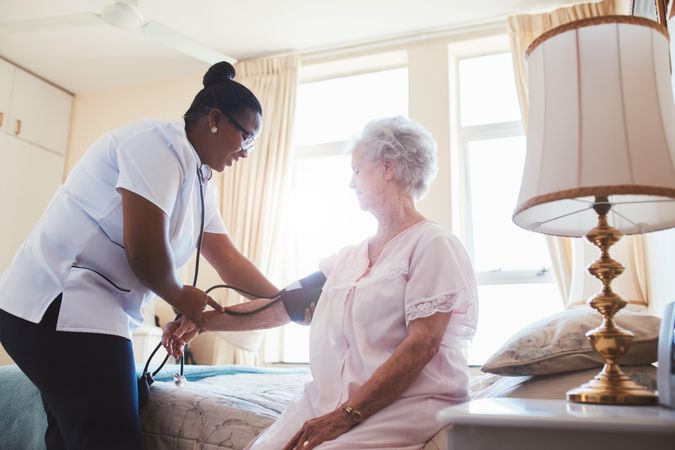 Female nurse doing blood pressure measurement of older woman patient