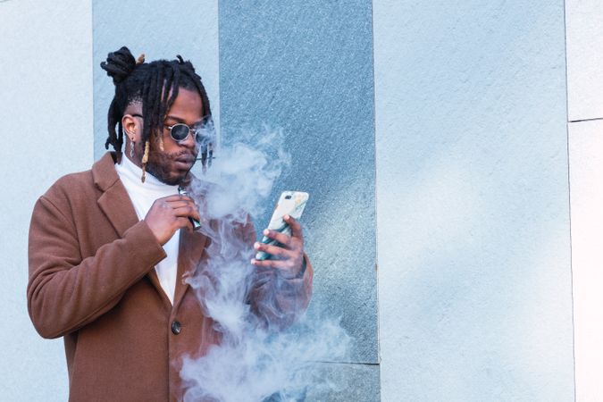 Cheerful Black man with electronic cigarette using mobile phone
