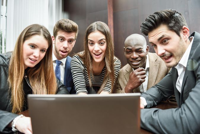 Male and female colleagues gathered around a laptop and smiling