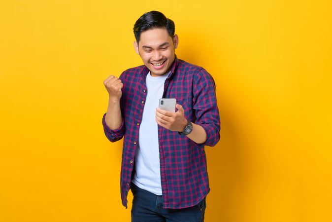 Asian man in plaid shirt excited  looking down at smartphone