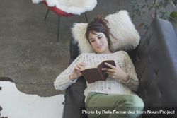Above view of female lying back reading book on leather sofa bD9QE0
