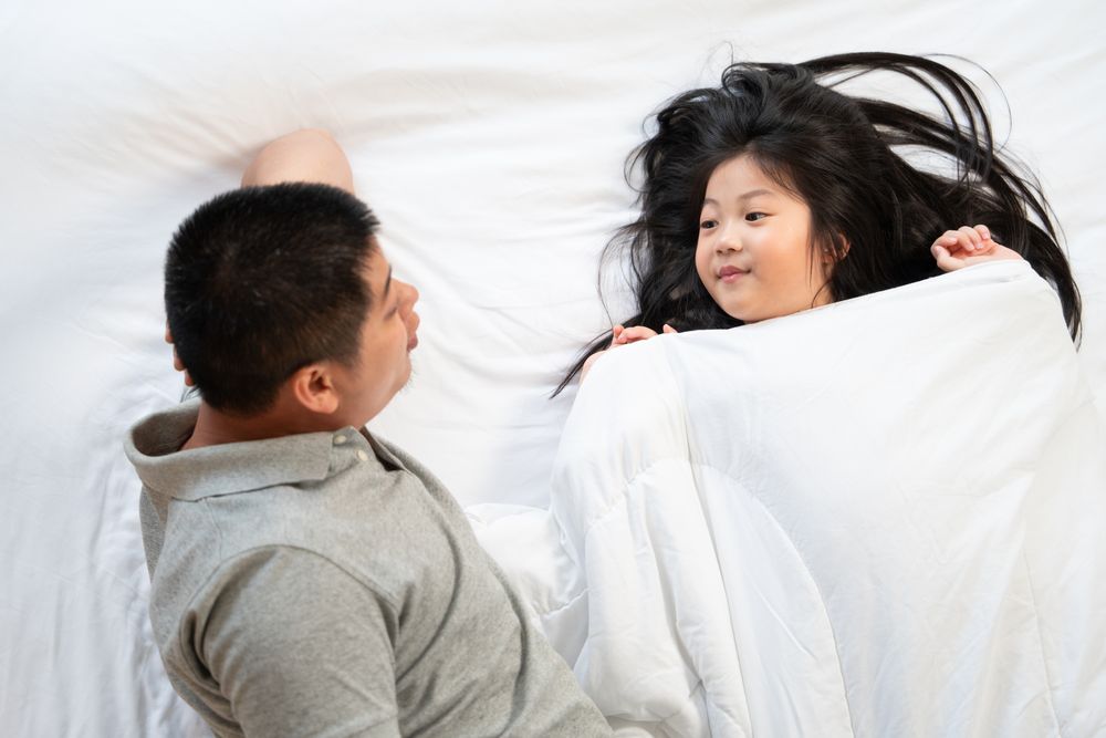 Asian father and daughter talking on bed.