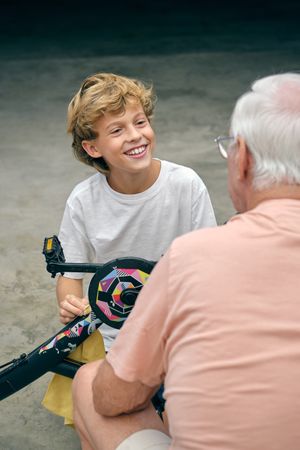 Cheerful grandson looking at grandfather while fixing bicycle