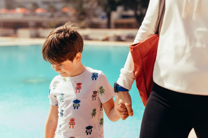 Young boy walking with woman at poolside
