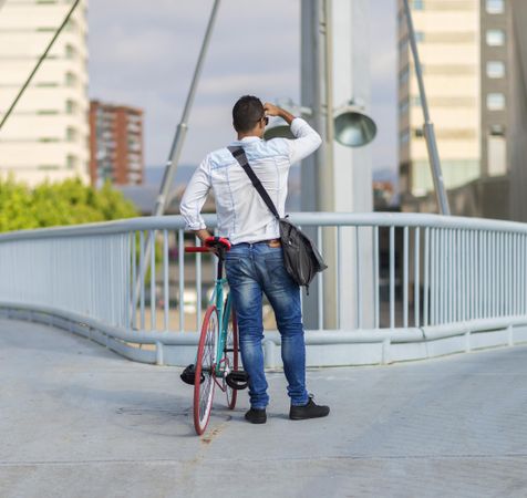 Back of male with bike looking over city view from bridge