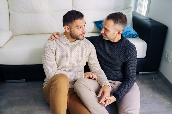 Cute male couple holding each other sitting on floor at home