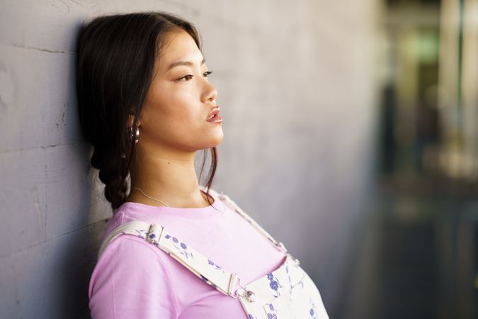 Female wearing casual clothes leaning against concrete wall, copy space