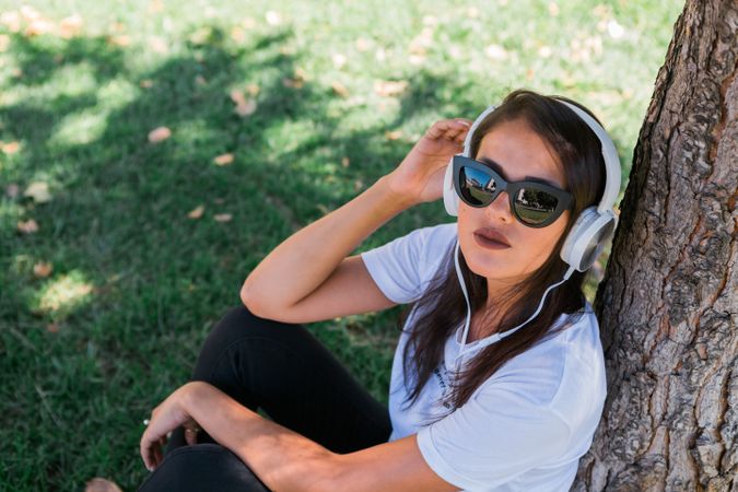 Relaxed trendy woman in headphones resting in park on grass