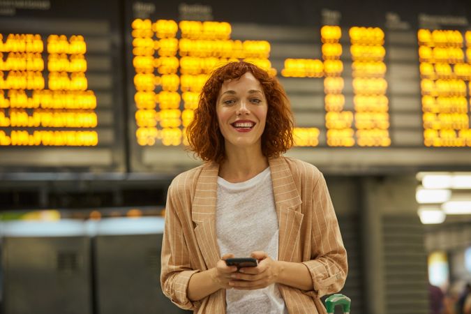 Red haired young woman using smartphone at station