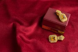 Beautiful shiny golden earrings with diamond studded Indian traditional design on a red velvet background
