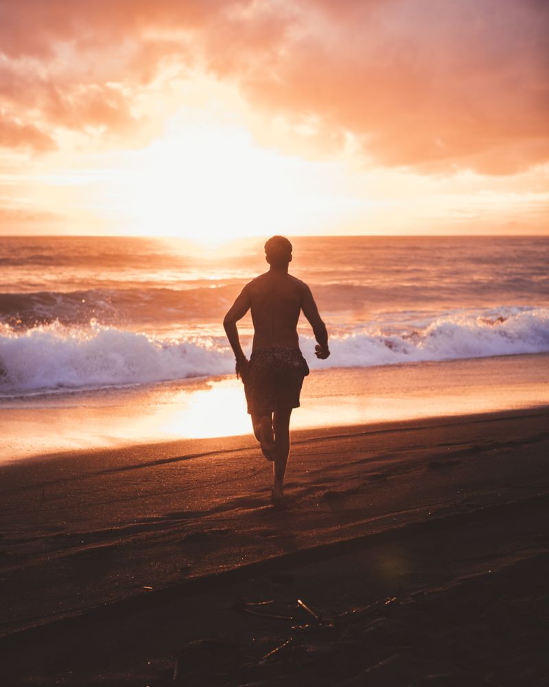 Running man on ocean shore in sunset