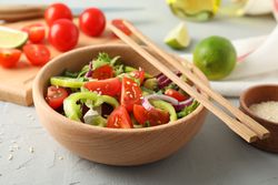 Fresh salad with chopsticks and kitchen accessories on grey background, close up