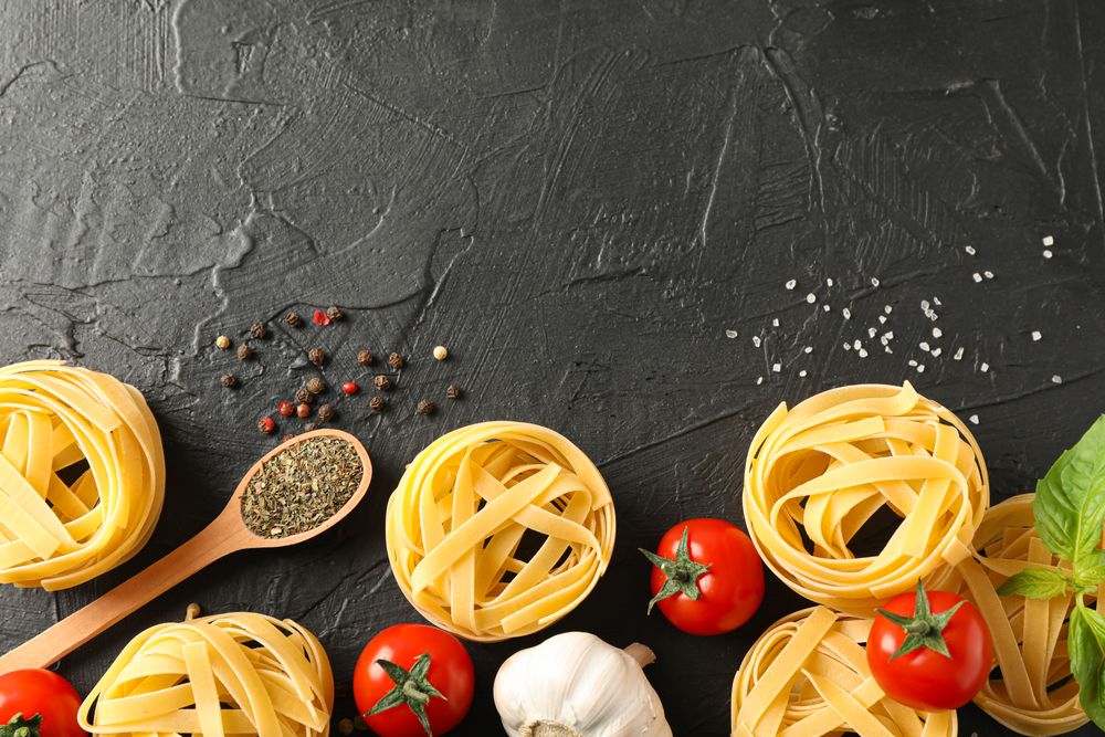 Flat lay composition with pasta, tomatoes, salt, garlic and spices on dark background, space for text
