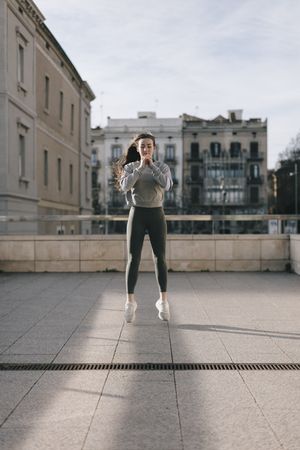 Front view of young woman exercising and jumping on a rooftop in the city