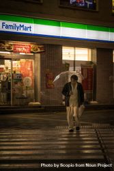 Man in dark jacket holding umbrella walking on sidewalk at night 5XJGMb