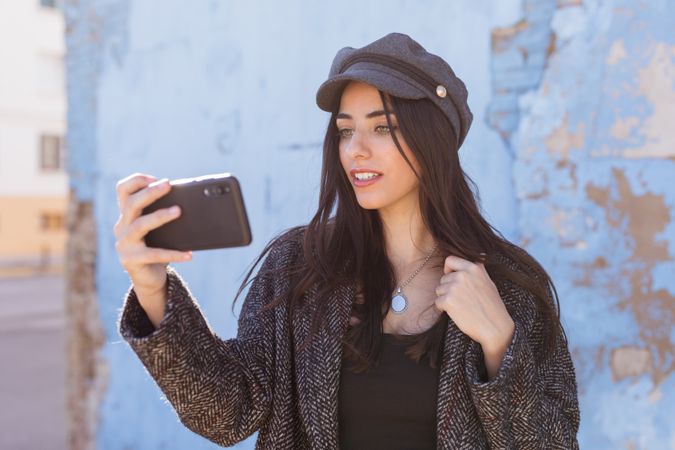 Charming Hispanic lady taking selfie near wall
