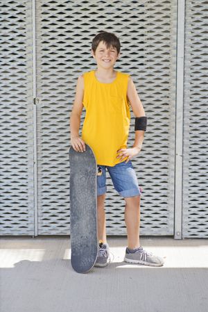 A teenage boy posing with skateboard and smiling
