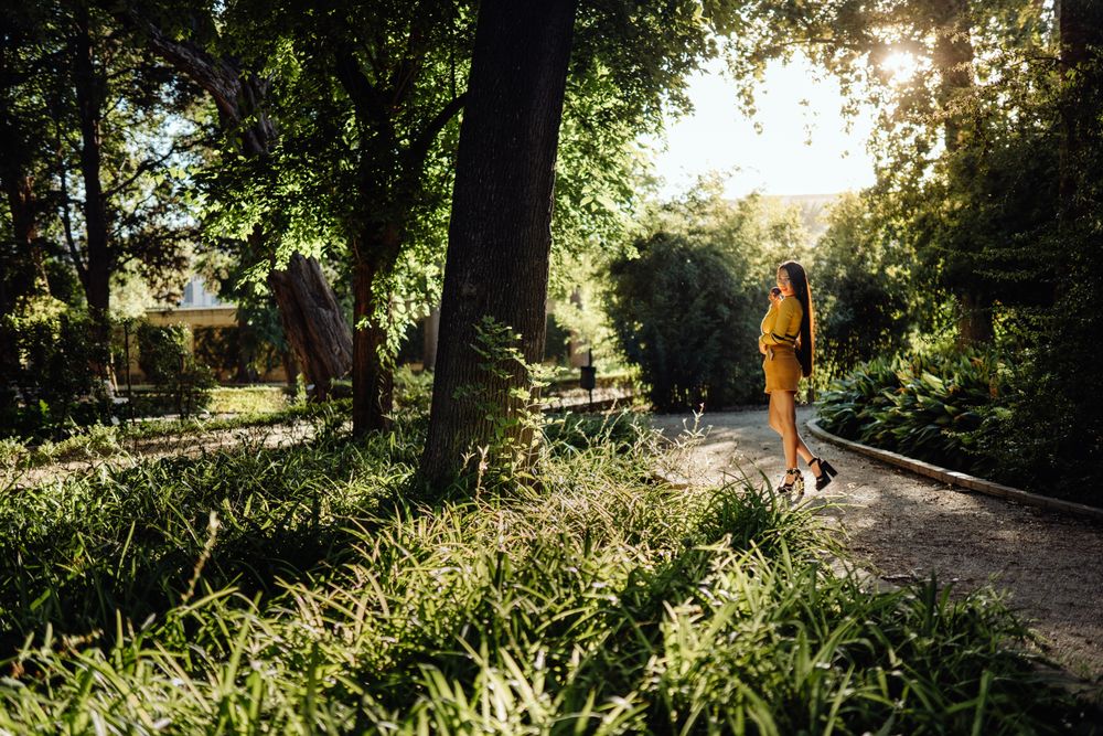Stylish long haired Asian woman walking in sunny alley in park