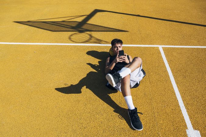 Male basketball player using his smartphone resting after training