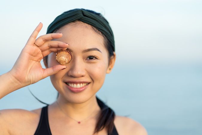 Happy Asian woman covering eye with sea shell