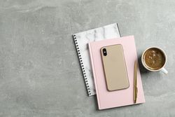 Cup of coffee with copybooks, phone and pen on grey background, top view