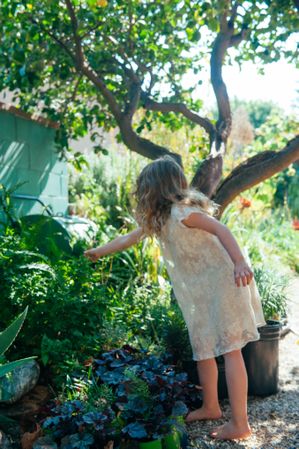Young girl wearing a dress reaching for a plant in her garden