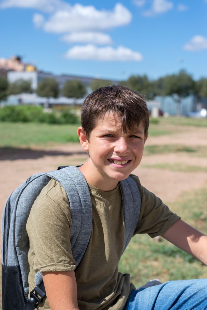 Happy boy sitting on outside wearing backpack