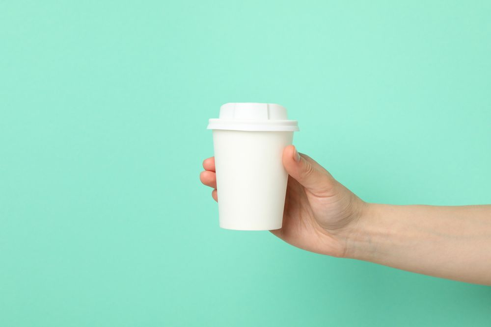 Female hand holds paper cup on mint background, space for text