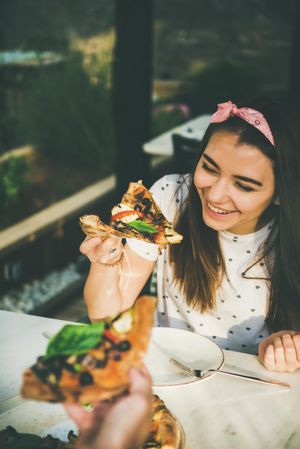 Couple eating pizza al fresco with wine, woman smiling holding pizza