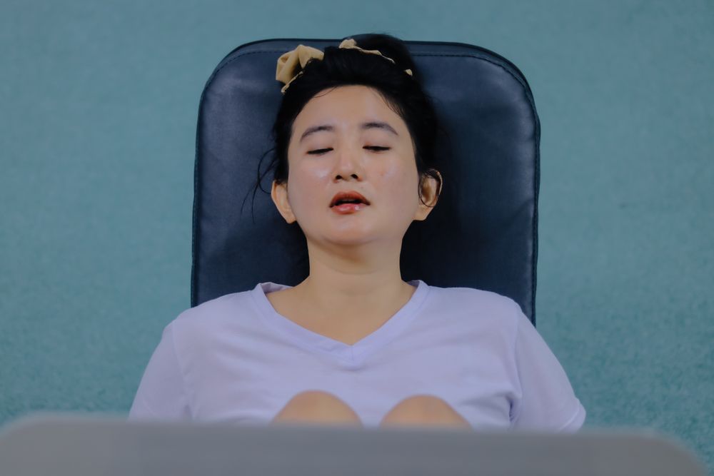 A woman is shown from the chest up, sitting and resting on a fitness machine.