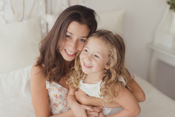 Mother ticking little daughter and laughing on bed