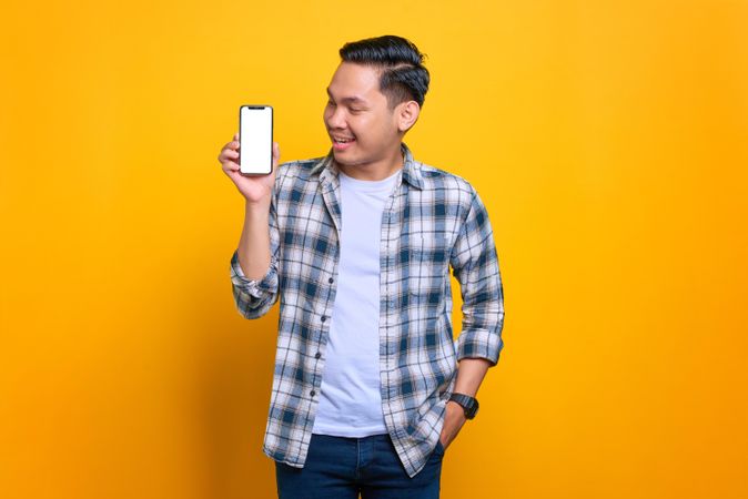 Smiling Asian male looking at smart phone with blank screen