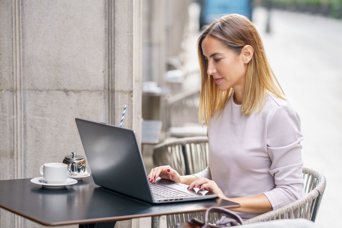 Woman sitting on cafe table outside with laptop