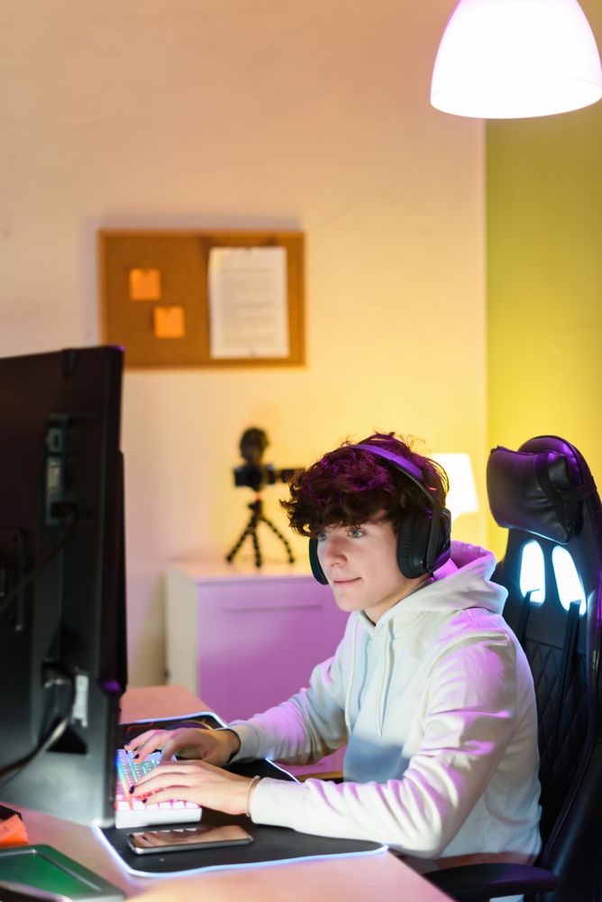 Young man in headphones playing on keyboard and sitting at table with gadgets