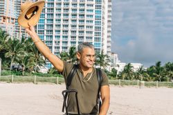 Happy male tourist in a clothes waving his hat to someone on the south beach.