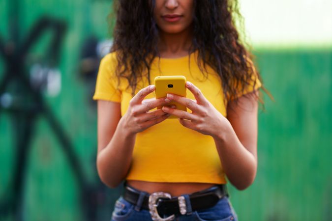 Cropped picture of woman in yellow t-shirt and jeans texting on phone