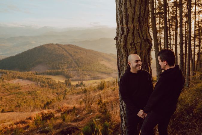 Smiling men hugging near tree in forest on hill