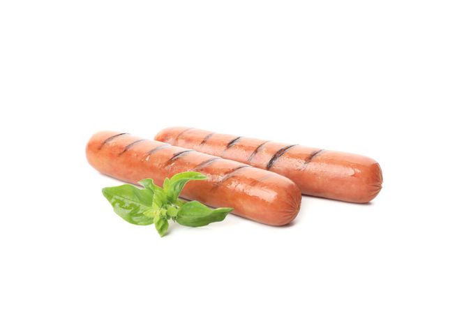 Two sausages with grill marks and garnish, side view