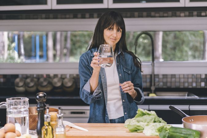 woman looking at camera while she shows a glass of water. Healthy lifestyle