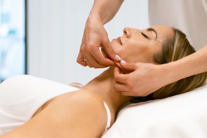 Side view of woman having her jawline massaged by massage therapist