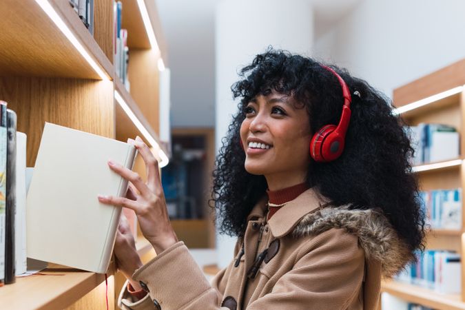 Satisfied woman with headphones taking book in library