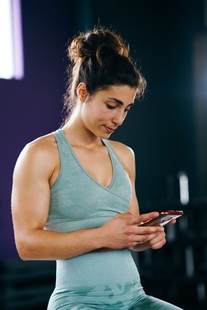 Woman looking down at her phone in gym, vertical